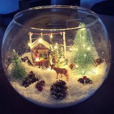 a glass bowl filled with snow and christmas decorations on top of a table next to a lit up house