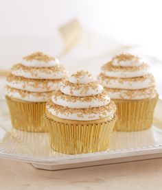 three cupcakes with white frosting and gold sprinkles on a plate