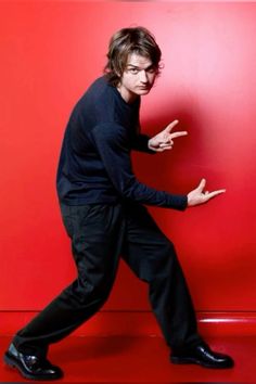 a man in black is leaning against a red wall with his hand on the floor