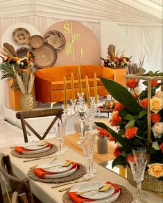 a dining table set with place settings and orange napkins on it, next to an orange couch