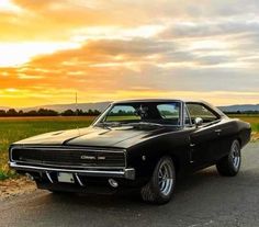 an old black muscle car parked on the side of the road in front of a field