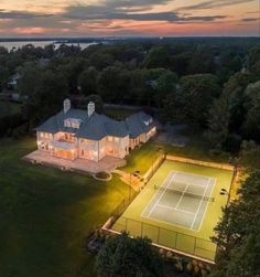 an aerial view of a tennis court and house at dusk with the sun setting in the background