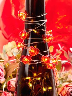 a bottle with some lights on it sitting in front of flowers and red paper roses