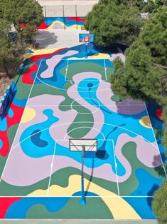 an aerial view of a basketball court painted in multicolored colors with trees surrounding it