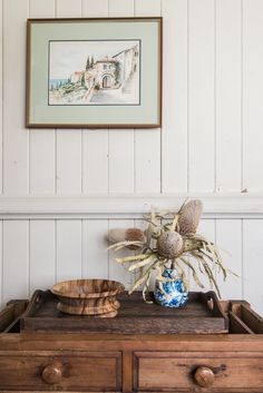 a wooden table with a blue and white vase on top of it next to a painting