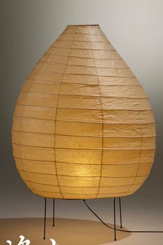 a large yellow paper lantern sitting on top of a metal stand next to a white wall