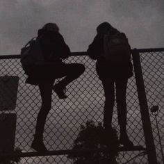 two people with backpacks are standing on a fence