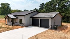 a two car garage sits in the middle of a dirt lot with trees behind it