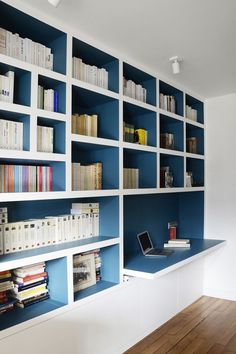 a bookshelf filled with lots of books next to a laptop on top of a wooden floor