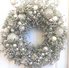 a christmas wreath with silver ornaments hanging on the front door, decorated with white and silver baubles