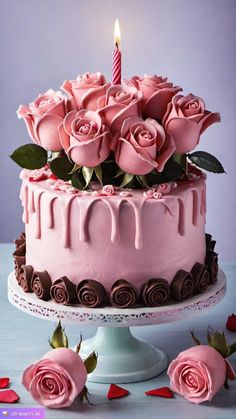 a cake with pink frosting and roses on it is sitting on a table next to two candles