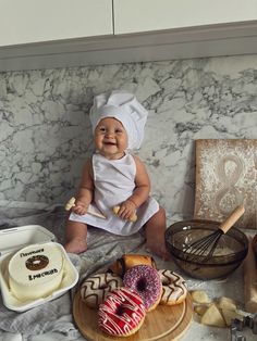 a baby sitting on top of a counter next to doughnuts