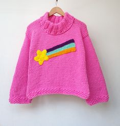 a pink sweater with a yellow flower on the front and a rainbow patch on the back