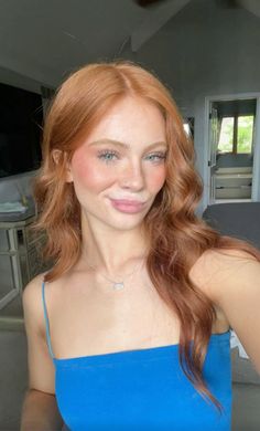 a woman with red hair is smiling and looking at the camera while wearing a blue top