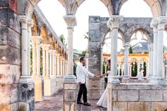 a bride and groom holding hands in an old building with arches on both sides, looking at each other