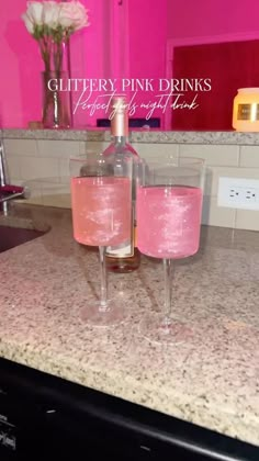 two wine glasses sitting on top of a counter next to a bottle and pink liquid