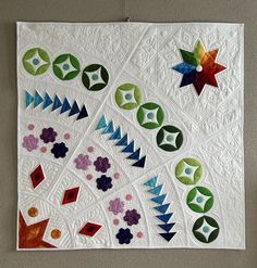 a quilted wall hanging on the side of a wall with many different colors and shapes