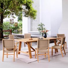 a wooden table with chairs around it in front of a tree and bushes on the ground