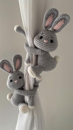 two crocheted rabbits hanging from a white curtain with an arrow in the middle