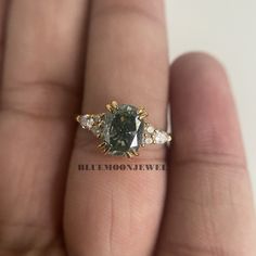 a close up of a person's hand holding a ring with a green and white diamond