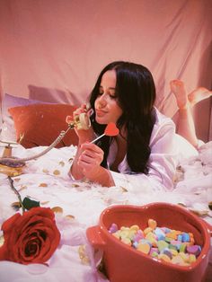 a woman laying in bed eating candy and holding a spoon with one hand while the other holds a rose