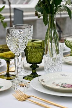 the table is set with plates, glasses and flowers in vases on top of them