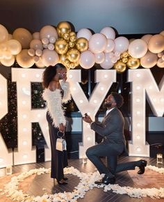 a man kneeling down next to a woman on a stage with balloons and streamers