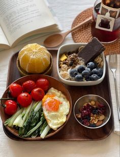 a tray filled with different types of food on top of a wooden table next to an open book