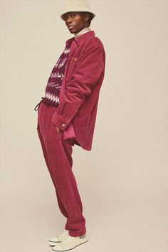 a man in a red suit and hat standing on a white background with his hands in his pockets