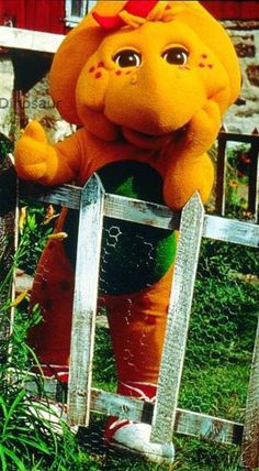 an orange elephant standing on top of a wooden fence next to a green planter