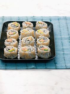 there are many sushi rolls on the black plate and blue place mat next to it