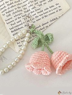 two crocheted flowers are next to a pearl bead necklace on a book page