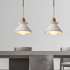 two pendant lights hanging over a dining room table with chairs and a gray wall in the background