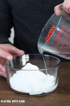 someone pouring sugar into a glass bowl on top of a wooden table with other ingredients