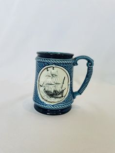 a blue and white mug with a ship on it's side, sitting against a white background