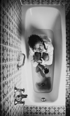 a woman sitting in a bathtub with her hands on the water and looking at the camera