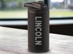 a black insulated water bottle sitting on top of a wooden table next to a window