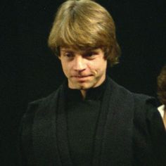 a man in a black suit and tie standing next to another man with brown hair