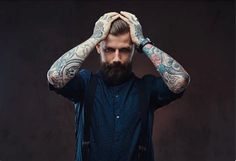 a man with tattoos holding his hands up to his head while standing in front of a dark background