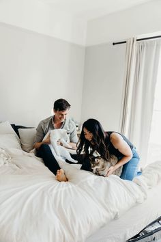 a man and woman sitting on top of a bed with a cat in their lap