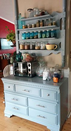 a blue dresser with shelves filled with dishes and cups on it's top shelf