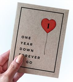 someone holding up a card with a heart balloon on it that says one year down forever go