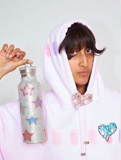 a woman in a pink hoodie holding up a silver bottle with hearts on it