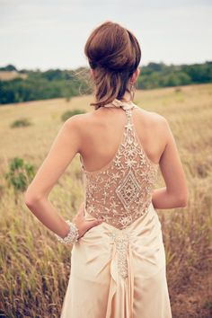 a woman standing in a field with her back to the camera, wearing a beige dress