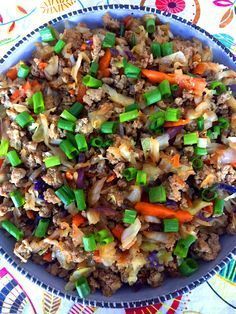 a blue bowl filled with meat and veggies on top of a colorful table cloth