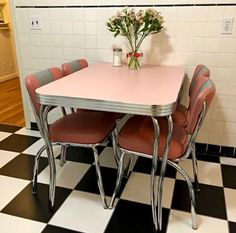 a pink table and four chairs in a room with black and white checkered floor