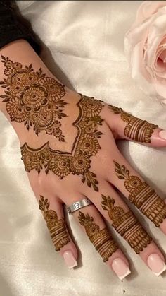 a woman's hand with henna on it and a rose in the background