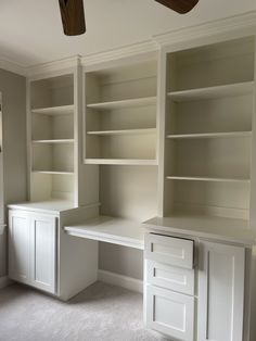 an empty room with white shelves and drawers in the corner, including a ceiling fan