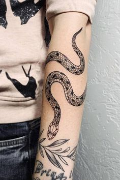 a woman's arm with tattoos on it and a snake tattooed on the arm