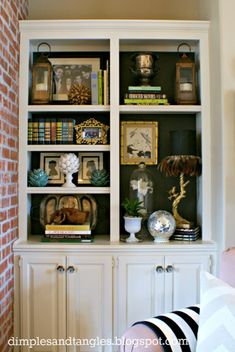 a white bookcase with books and pictures on the top, sitting in front of a brick wall